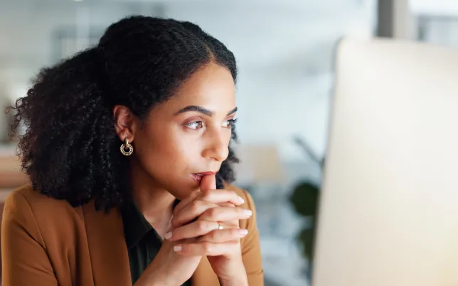 Woman at computer in office, thinking.