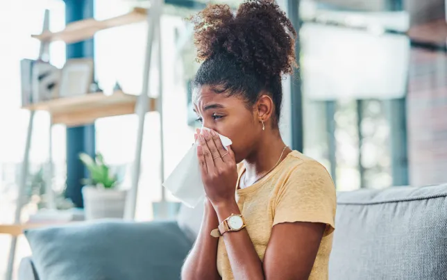 Shot of a young woman feeling ill and blowing her nose sitting on the sofa at home.