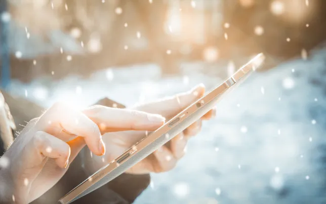 Close-Up of a man's hands holding up and looking at a tablet in a snowstorm.