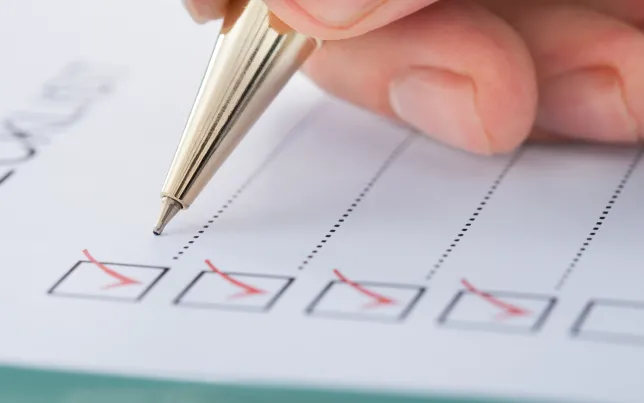 Close-up of a hand holding a pen checking off boxes on paper.
