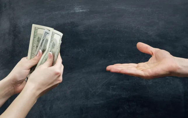 Close-up of two hands. One hand holding dollar bills and the other hand is open/outstreched asking for money.