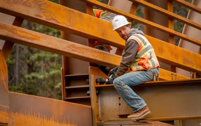 Construction worker sitting on a beam while working on a bridge construction job.