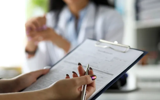 Female visitor filling out medicine documents in doctor office.