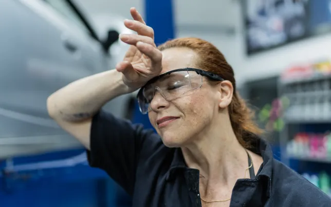 Close up of a tired and hot female factory worker wiping sweat from her forehead.