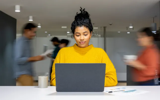  Businesswoman working on her laptop at a busy office.