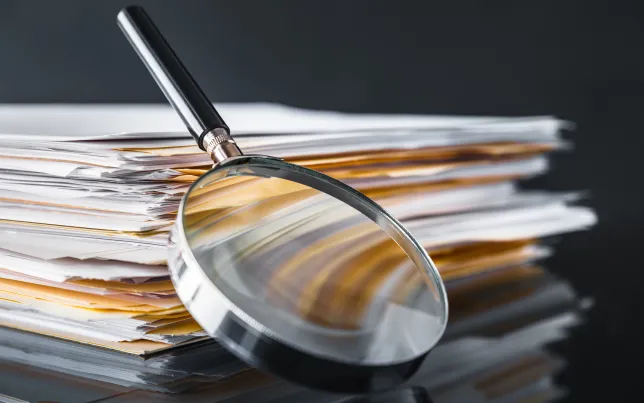 A magnifying glass leaning against a pile of files and documents.