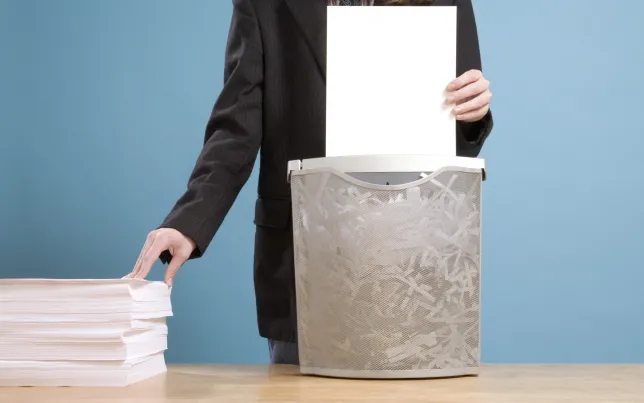 Close-up of a man feeding paperwork from a large pile into a shredder.