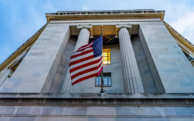 Upview of the facade of the U.S. Department of Justice building with an American Flag waving in front.