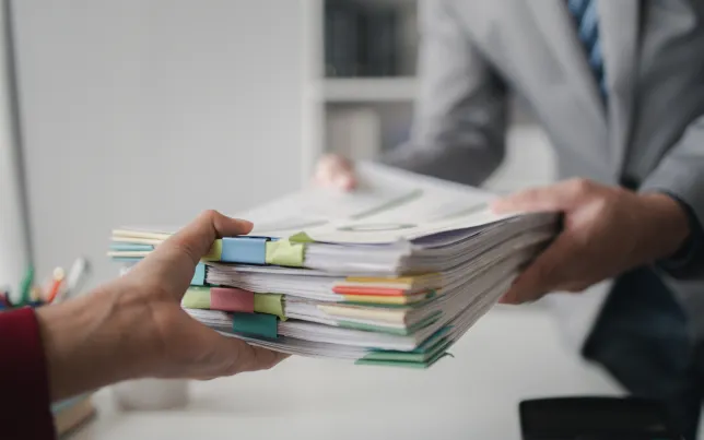 Close-up of hands: two company employees handing over papers to each other.