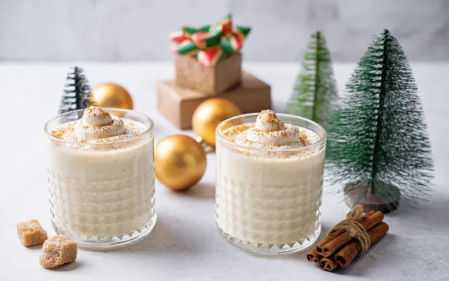 Two glasses of coquet (or eggnog) surrounded by cinnamon and holiday decorations.
