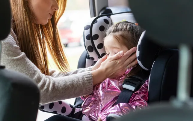 Mother putting her sick child in a car seat to go to doctor's office.