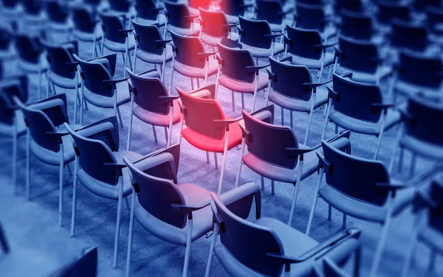 Single red chair highlighted among rows of empty seats, symbolizing individuality, selection, recruitment or standout position in a group.