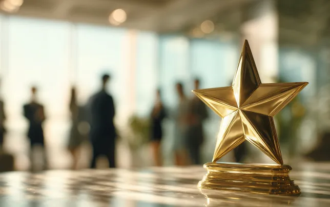 Close-up of a gold star award in foreground and blurred office employees in background.