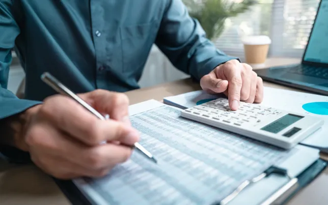 Person using calculator and reviewing financial documents for accounting and budget planning.