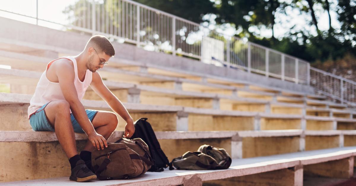 A college student, male, sitting on bleachers in his workout clothes, looking through his gym bag.