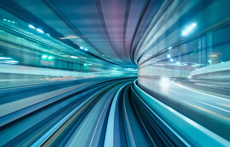 Panorama of motion blurred high speed train driving along the rails through an illuminated tunnel at night.