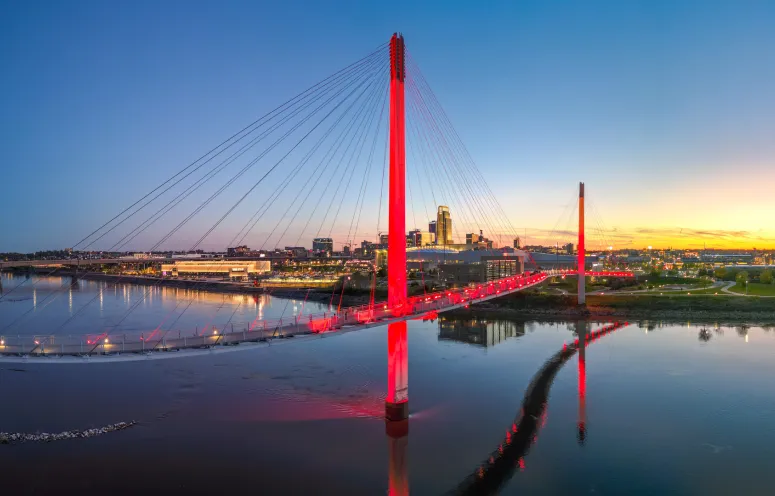 Skyline of Omaha, Nebraska at dusk with the Bob Kerrey Pedestrian Bridge illuminated.